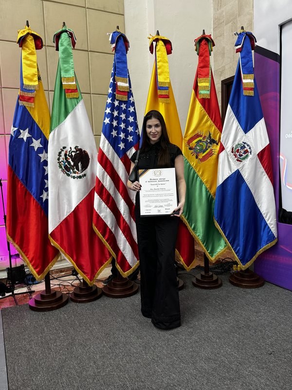 Dra. Amanda Vitorino segurando um certificado em frente às bandeiras de países participantes